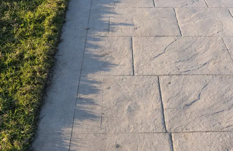 Acera de hormigón impreso junto a zona verde — Huelva Acera de hormigón impreso imitación losa de piedra bordeando el césped de una urbanización en Huelva