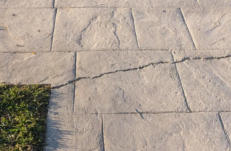 Camino de hormigón impreso imitación losa de piedra con una junta abierta y el sellado desgastado en un jardín de Huelva