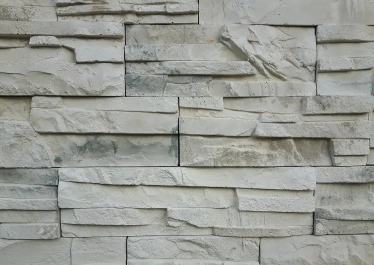 Zócalo de fachada revestido con hormigón imitación muro de piedra apilada en color hueso en Isla Cristina, Huelva